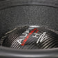 Gros plan sur un cône de haut-parleur Helon H15 EVO2 en fibre de carbone noire de la marque Audio System, avec le logo blanc et rouge sur le cache-poussière du caisson de basses de 15 pouces.