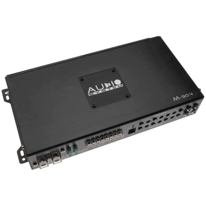 The Audio System M-90.4 is a black rectangular 4-channel car audio amplifier with multiple ports, labeled AUDIO SYSTEM on top.