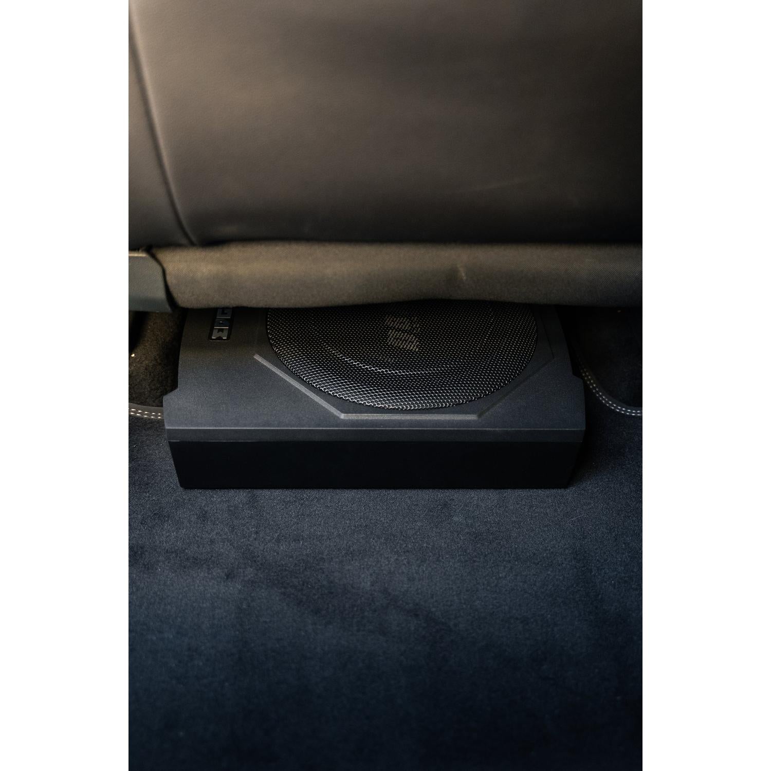 El Edge Car Audio EDBX10A-E0 es un subwoofer ultraplano negro de 10 Zoll instalado debajo de un asiento de coche sobre moqueta oscura.