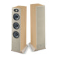 Una coppia di diffusori Focal Theva N°3 in legno chiaro: uno con altoparlanti e tweeter a vista, laltro con rivestimento in tessuto beige - perfetti per unelegante configurazione home cinema.