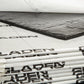 Une pile de panneaux Gladen Aero Silent Pro destinés à labsorption acoustique, avec un gros plan sur un panneau rectangulaire noir partiellement décollé.