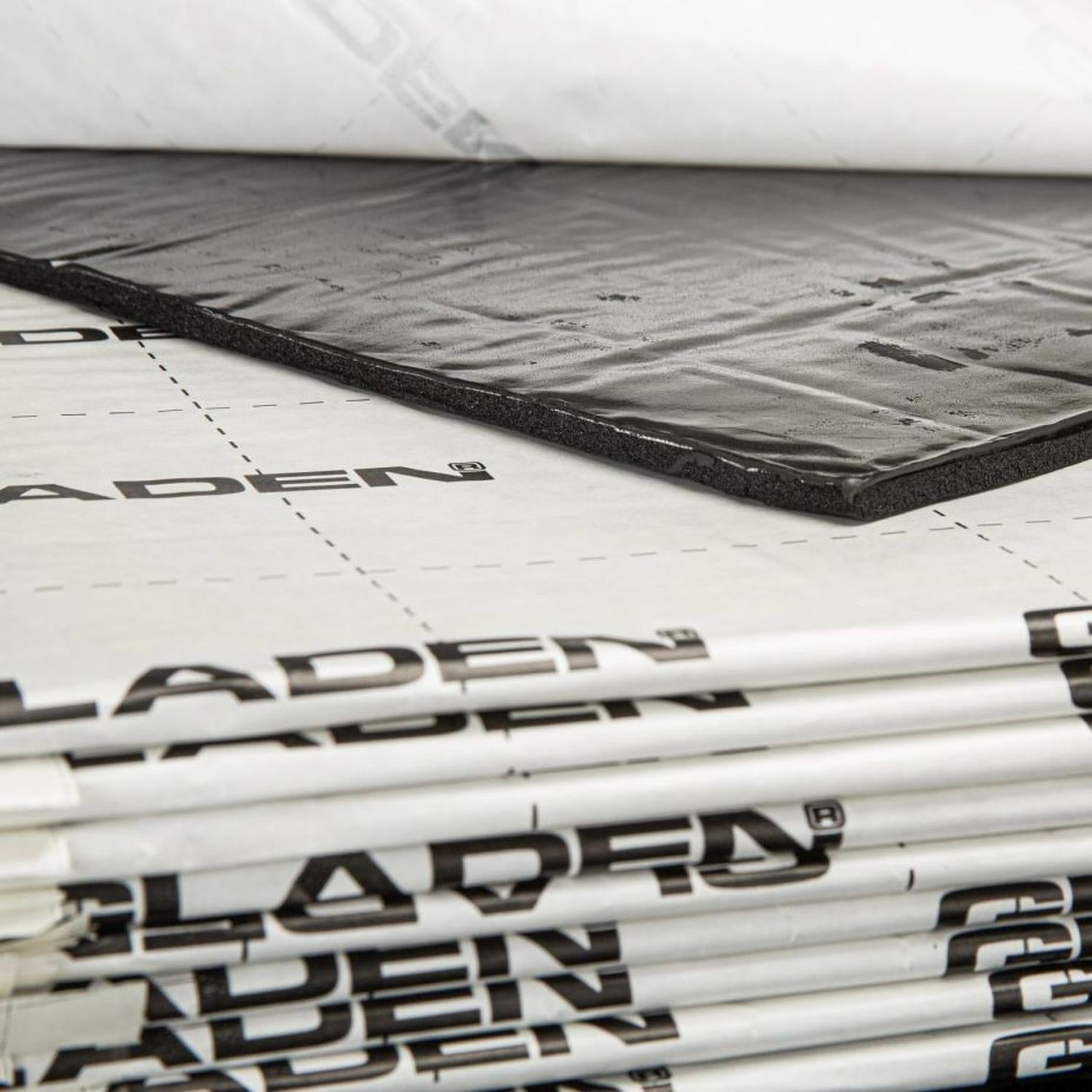 Une pile de panneaux Gladen Aero Silent Pro destinés à labsorption acoustique, avec un gros plan sur un panneau rectangulaire noir partiellement décollé.