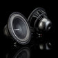 Dos subwoofers negros Aero 10 de Gladen Aerospace se encuentran sobre una superficie reflectante, uno orientado hacia delante y otro hacia atrás, lo que pone de relieve su estilo «Auto Hifi» de alta gama.