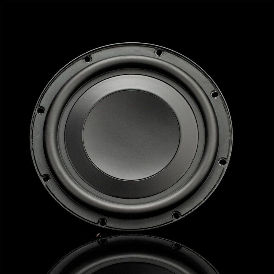 Un subwoofer Gladen GS08 Slim negro, de diseño redondeado, está situado en el centro de un fondo oscuro, cuyo reflejo se ve debajo.