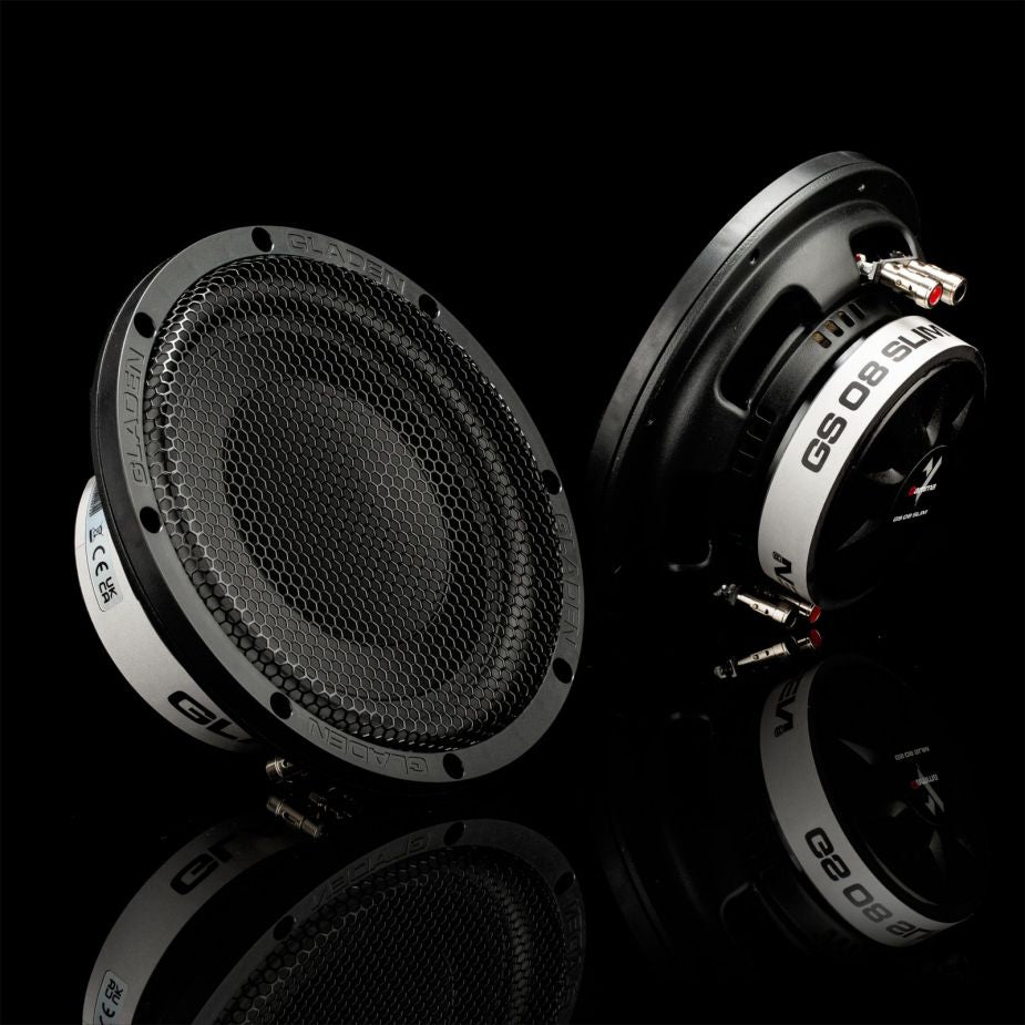 Se muestran dos subwoofers Gladen GS08-Slim de 8 pulgadas, en negro y plateado, con rejillas de malla, sobre una superficie negra brillante que refleja su imagen.