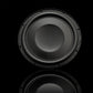 A Gladen GS10-Slim Subwoofer stands against a black background, its powerful bass suggested by a subtle reflection beneath its clear circular edge.