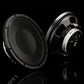Due subwoofer Gladen GS12-Slim – uno con griglia di protezione, l’altro inclinato in modo tale da rendere visibili il cablaggio e il logo – sono posizionati su una superficie nera lucida.