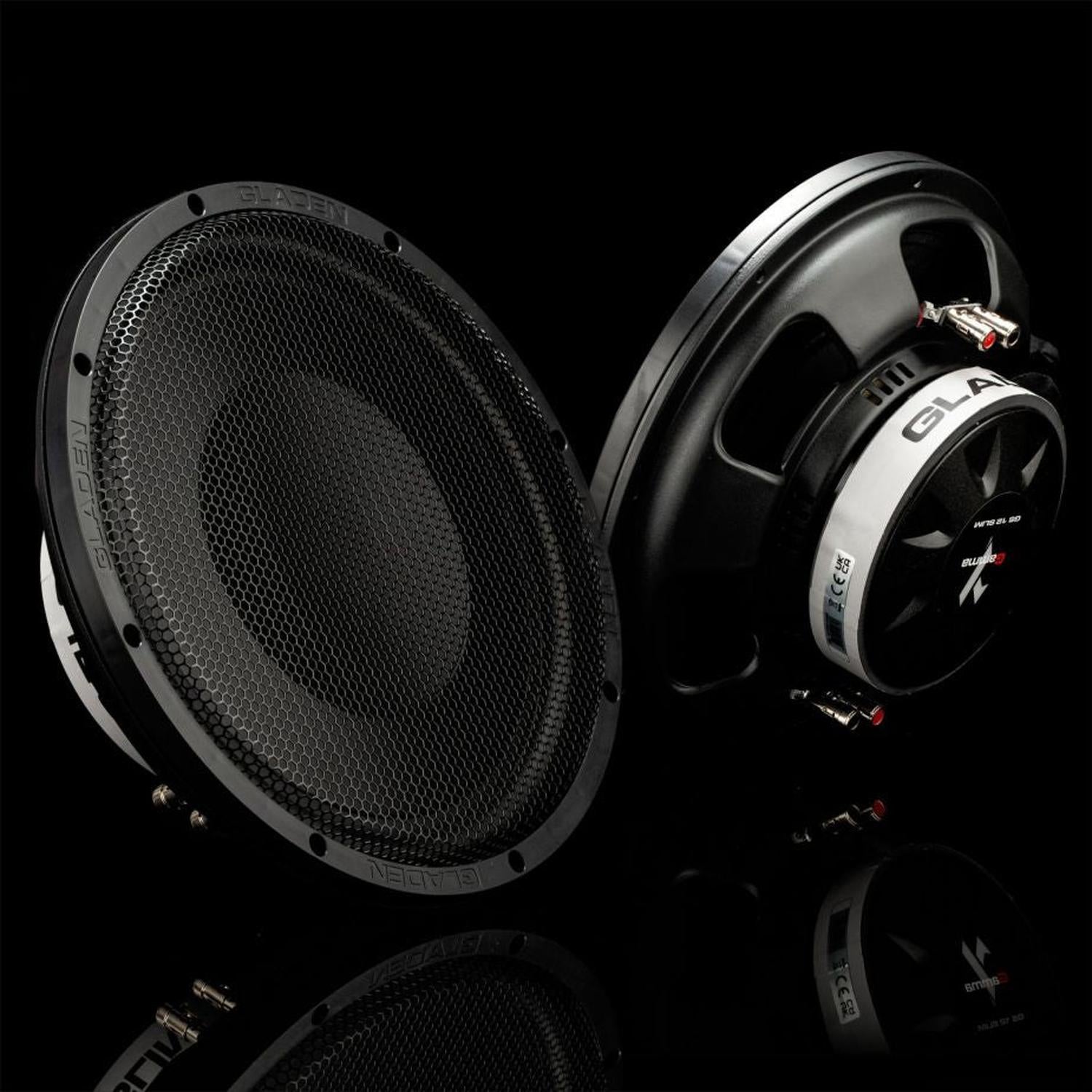 Due subwoofer Gladen GS12-Slim – uno con griglia di protezione, l’altro inclinato in modo tale da rendere visibili il cablaggio e il logo – sono posizionati su una superficie nera lucida.