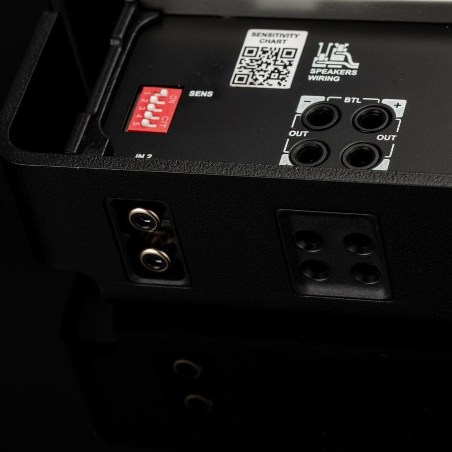 Primo piano di un amplificatore Gladen Mosconi Pro 1|10 evo che mostra le porte di ingresso/uscita, la tabella di sensibilità, lo schema di cablaggio e gli interruttori DIP rossi su una superficie nera.