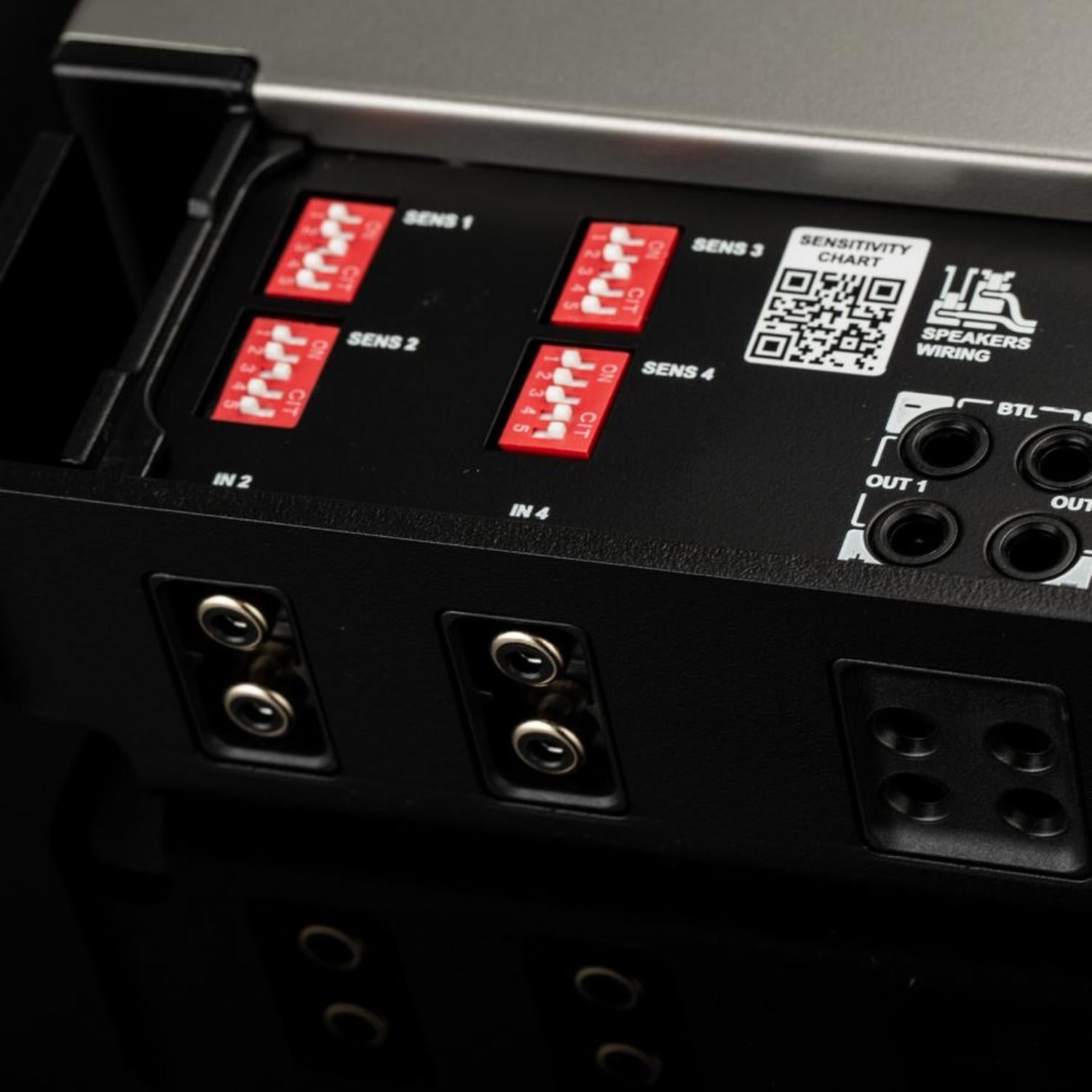 Primo piano del pannello di controllo dellimpianto audio per auto «Gladen Mosconi Pro 4|10-AAB EVO» con interruttori rossi, scala di sensibilità, quattro ingressi ed etichette per il cablaggio.