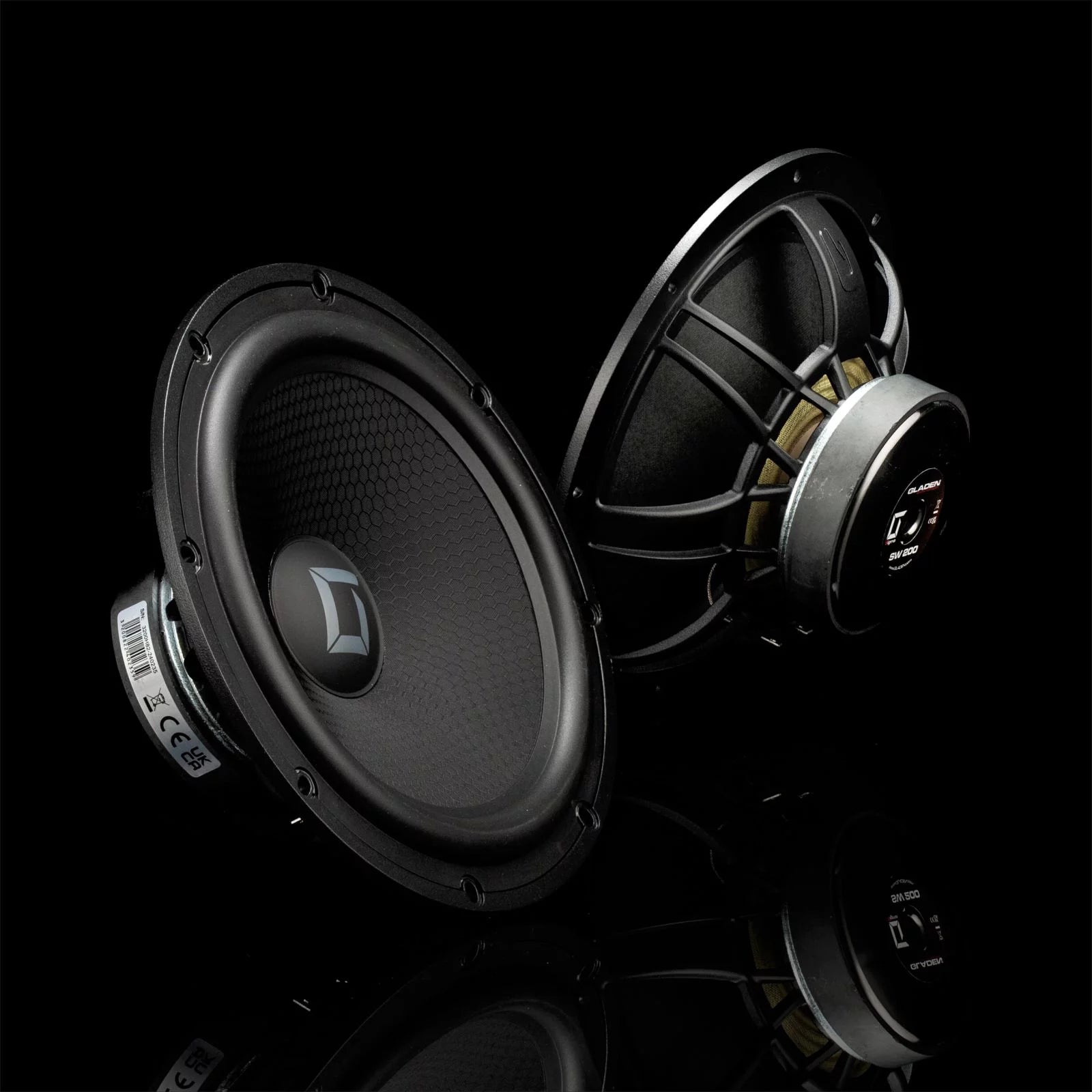 Deux enceintes Gladen Sigma 200 noires et rondes, dotées de cônes texturés et de cadres métalliques, sont mises en valeur sur un fond noir brillant.