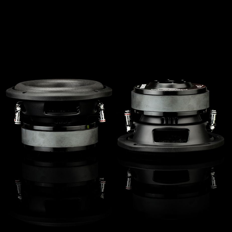 Se muestran dos subwoofers Gladen Sigma SSW065 en color negro, ideales para instalaciones en vehículos compactos: uno orientado hacia delante y el otro mostrando su parte trasera y lateral.