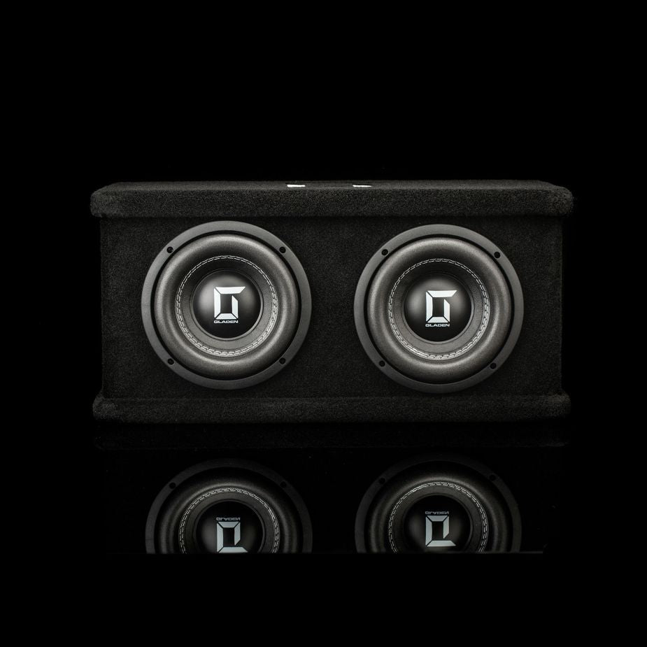 El Gladen Sigma SSW065 Dual, un subwoofer negro con dos altavoces de 6,5 y logotipos Sigma plateados, se presenta sobre un fondo oscuro con un sutil reflejo en la parte inferior.