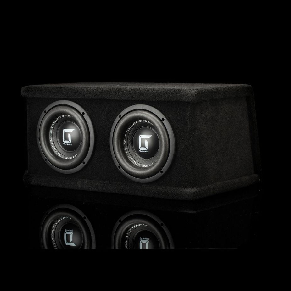 El Gladen Sigma SSW065 Dual cuenta con dos subwoofers de 6,5 en una elegante caja negra, expuestos sobre una superficie reflectante con fondo oscuro.