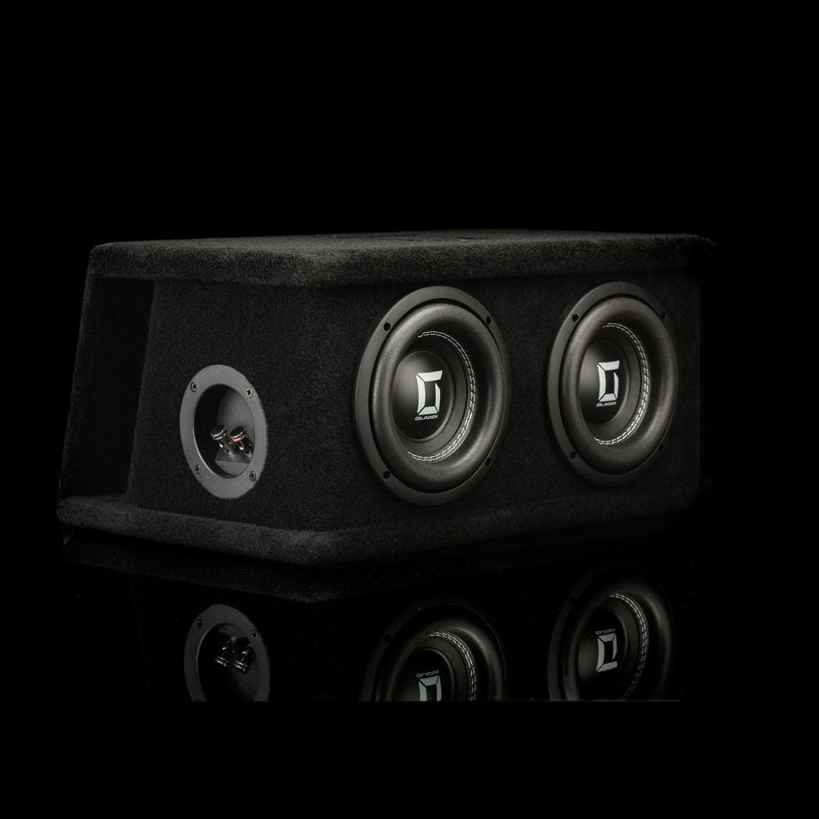 Il Gladen Sigma SSW065 Dual, un subwoofer con cabinet nero dotato di due altoparlanti da 6,5 pollici, poggia su una superficie lucida e mette in risalto lo stile Sigma su uno sfondo scuro.