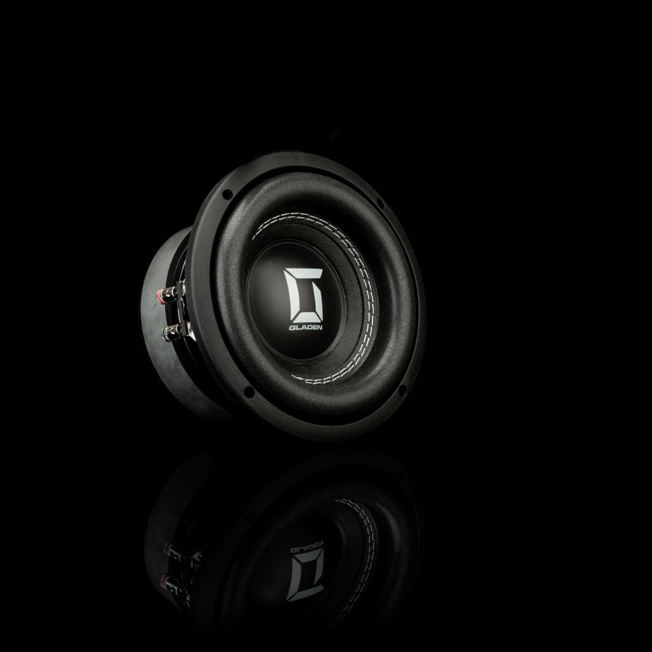 Un subwoofer Gladen Sigma SSW065 nero con il logo al centro, raffigurato su uno sfondo nero con un leggero riflesso nella parte inferiore.