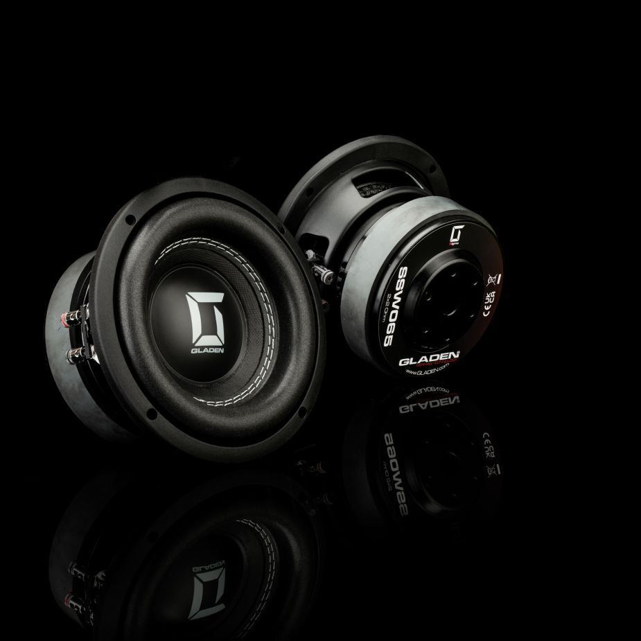 Due subwoofer Gladen Sigma SSW065 neri su una superficie nera riflettente; uno ne mostra la parte anteriore, l’altro ne rivela il retro nei minimi dettagli: ideali per installazioni su veicoli compatti.