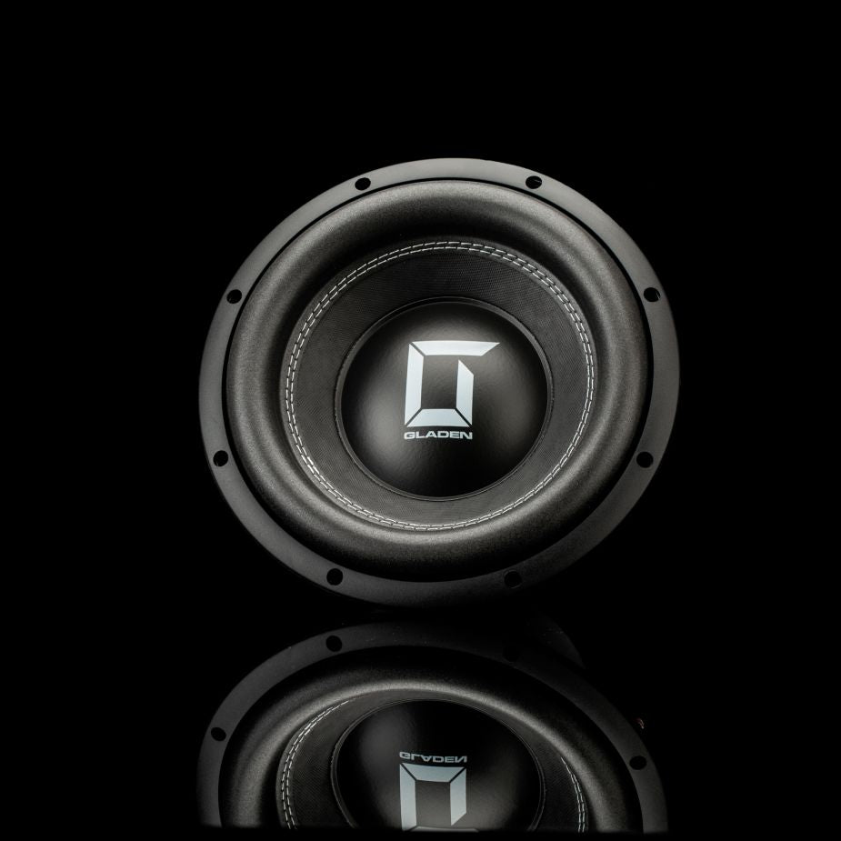 Un subwoofer Gladen Sigma SSW10 circular de color negro con un logotipo «G» plateado y la inscripción «Gladen» sobre un fondo negro, con un ligero reflejo en la parte inferior.