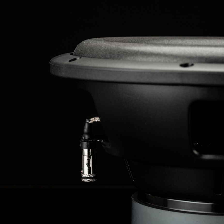 Primer plano de un subwoofer Gladen Sigma SSW10 sobre un fondo oscuro, en el que se aprecian su puerto de conexión y el cono texturizado del altavoz.