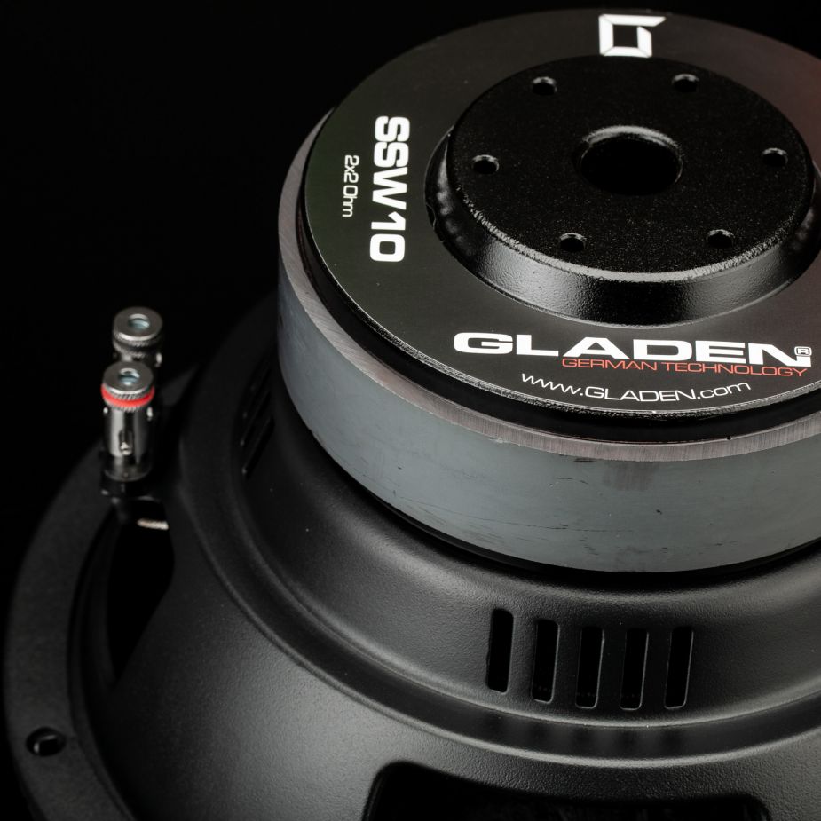 Primer plano del subwoofer Gladen Sigma SSW10, en el que se aprecian el logotipo de la marca, los terminales de conexión y el marco metálico sobre un fondo negro.