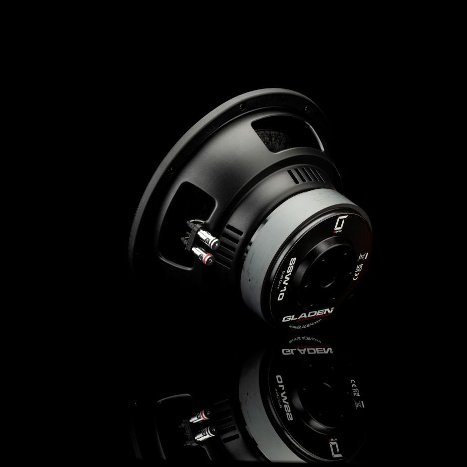 Un subwoofer Gladen Sigma SSW10, nei colori nero e argento, è appoggiato in posizione inclinata su una superficie nera lucida, con i terminali di collegamento ben visibili.