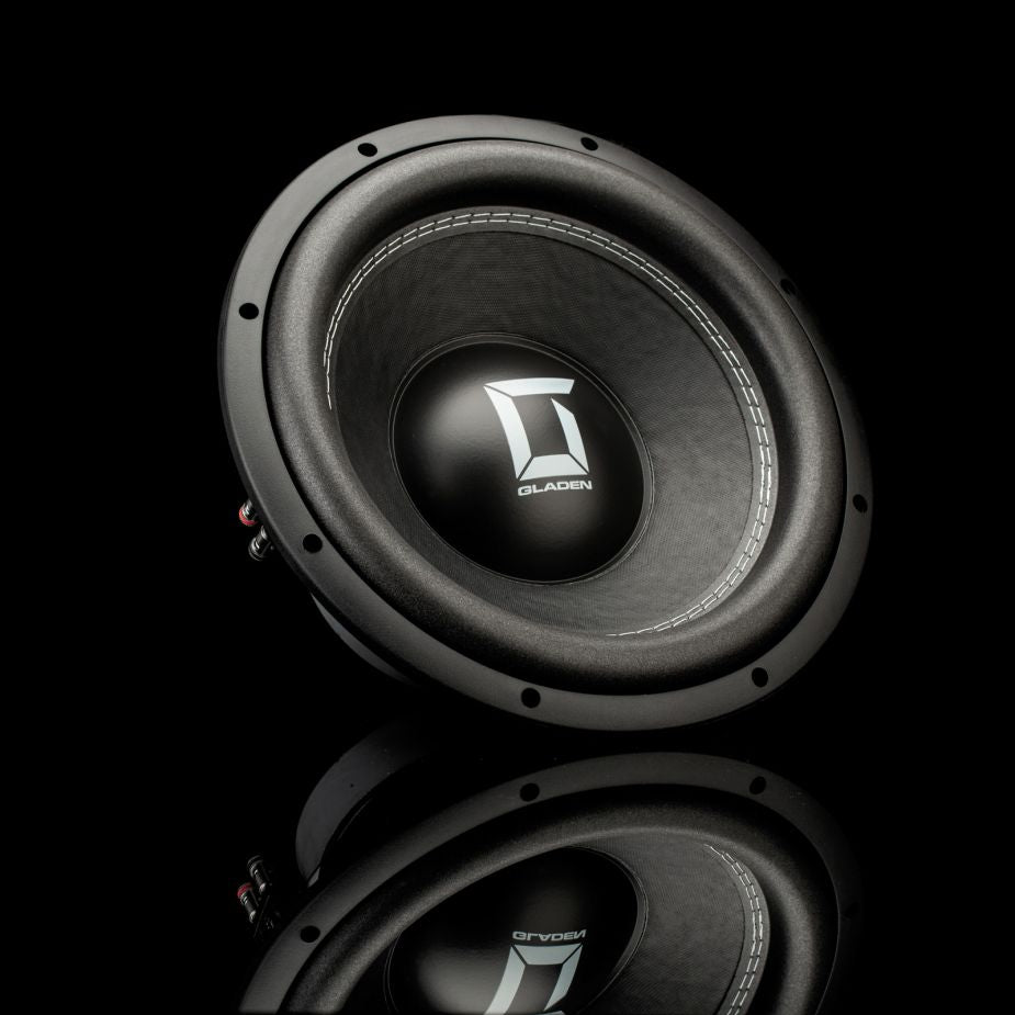 Un subwoofer Gladen Sigma SSW12 con acabado negro metalizado se exhibe sobre una superficie negra brillante, lo que resalta su diseño redondeado y su logotipo.