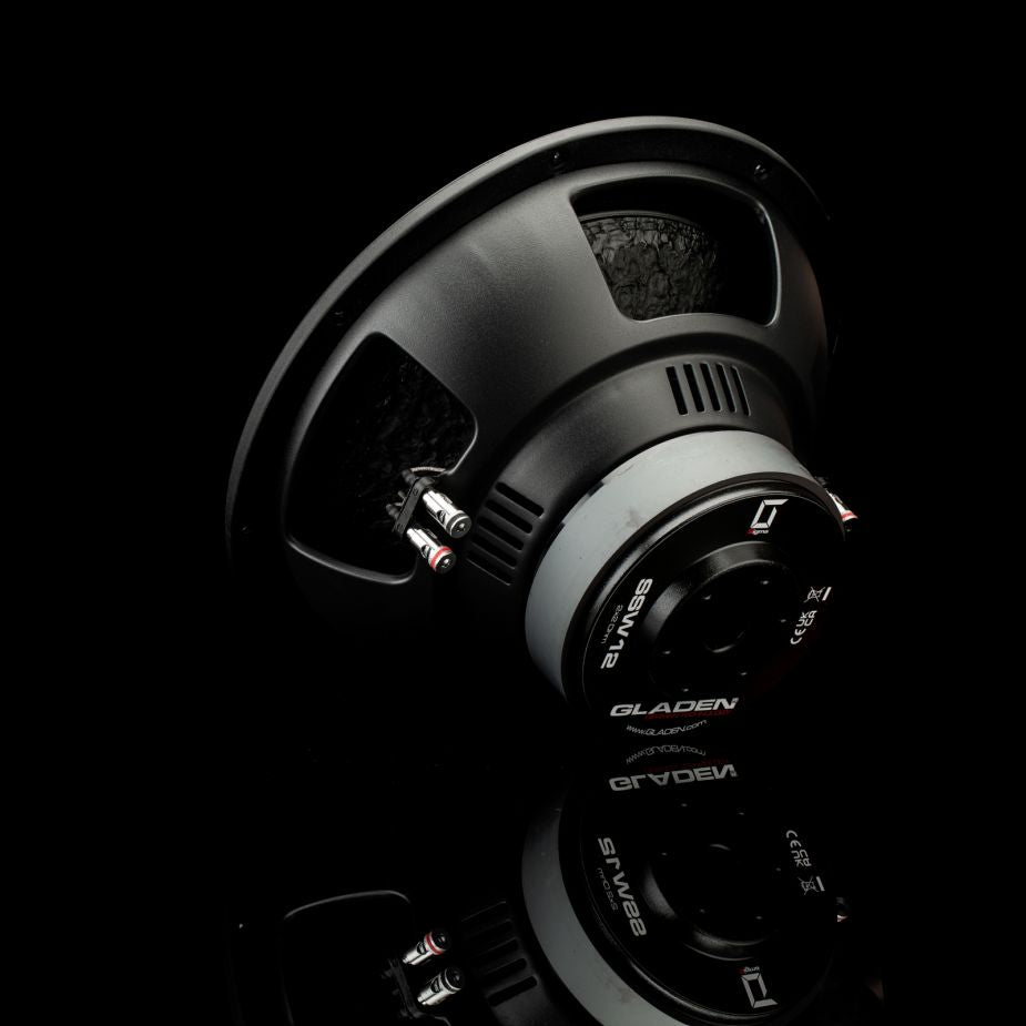 El Gladen Sigma SSW12 se presenta en ángulo, con sus detalles metálicos brillando sobre el fondo negro, lo que lo hace ideal para los graves profundos del sistema de audio del coche.