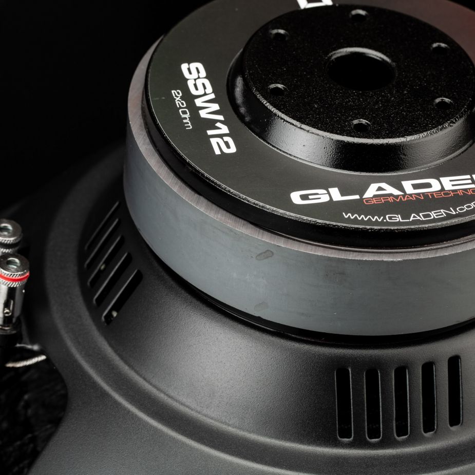 Primo piano del subwoofer per auto Gladen Sigma SSW12, che mostra le parti metalliche, letichetta e le aperture di ventilazione su uno sfondo scuro.