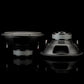 Due subwoofer Gladen Sigma SSW12 – uno rivolto in avanti, l’altro inclinato – si riflettono su una superficie lucida davanti a un elegante sfondo nero.