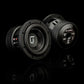 Due subwoofer Gladen Sigma SSWX065, ripresi frontalmente e posteriormente su una superficie riflettente, mostrano i loghi, i terminali di collegamento e i dettagli del modello, garantendo un’eccellente riproduzione dei bassi.