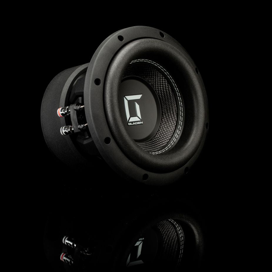 Un subwoofer Gladen Sigma SSWX08 nero, con cono testurizzato e cablaggio a vista, poggia su una superficie nera lucida che riflette il diffusore.