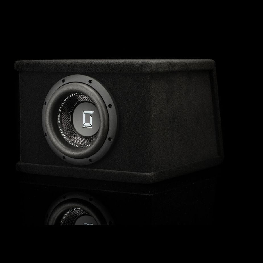 A black Gladen Sigma SSWX08VB 8 subwoofer in a rectangular enclosure sits on a reflective surface, with a silver logo centered on the speaker cone.