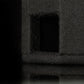 Primo piano di un Gladen Subbox-EV grigio scuro con finitura ruvida e porta quadrata, riflesso su una superficie lucida su sfondo nero.