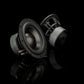 Dos subwoofers Gladen Zeta 08, elogiados por la precisión de sus graves, descansan sobre una superficie negra brillante con un espectacular fondo negro.