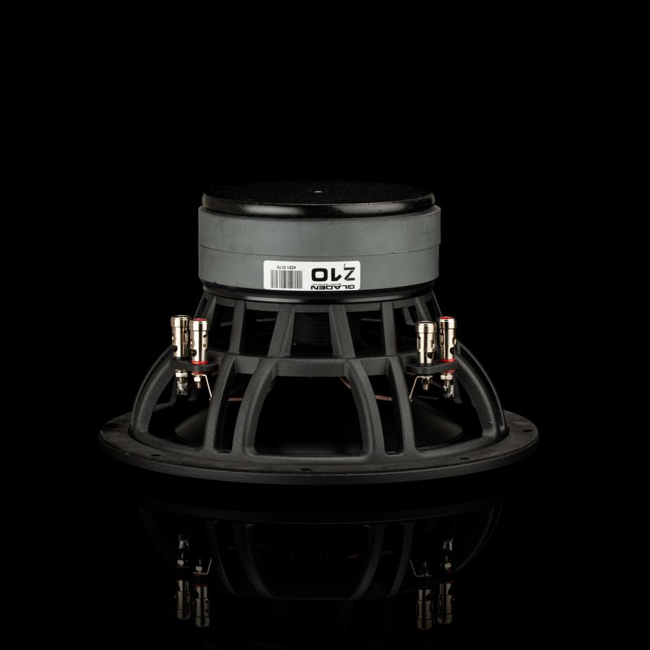 Un subwoofer Gladen Zeta 10, en negro y plateado, descansa sobre una superficie negra, en la que se aprecian una etiqueta con un código de barras y unos terminales de conexión, diseñado para ofrecer unos graves potentes.