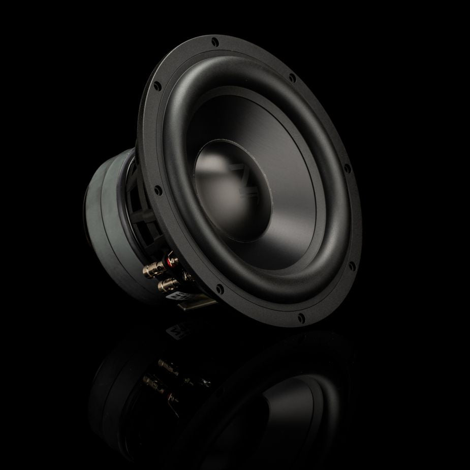 Un subwoofer Gladen Zeta 10 de color negro está colocado en ángulo sobre una superficie reflectante, dejando a la vista su cableado y los orificios de montaje, lo que lo hace ideal para una reproducción de graves profundos en tu equipo.