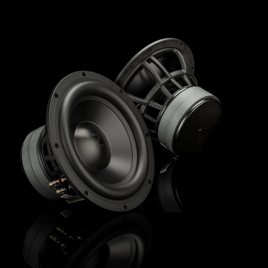 Due subwoofer Gladen Zeta 10, che garantiscono bassi potenti, sono posizionati su una superficie nera lucida davanti a uno sfondo scuro e minimalista.